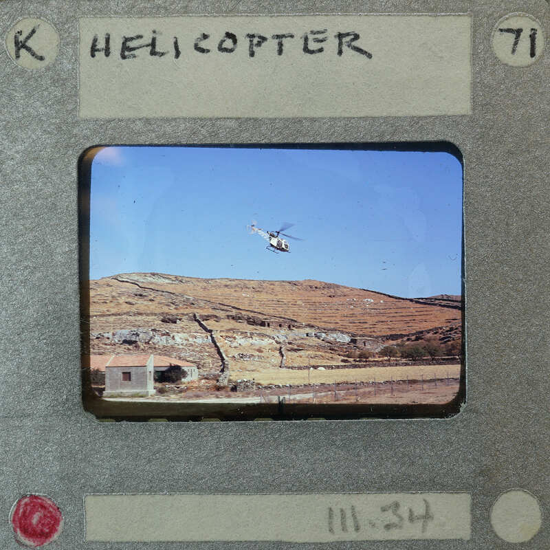 Helicopter flying over a mountainous landscape with houses below.