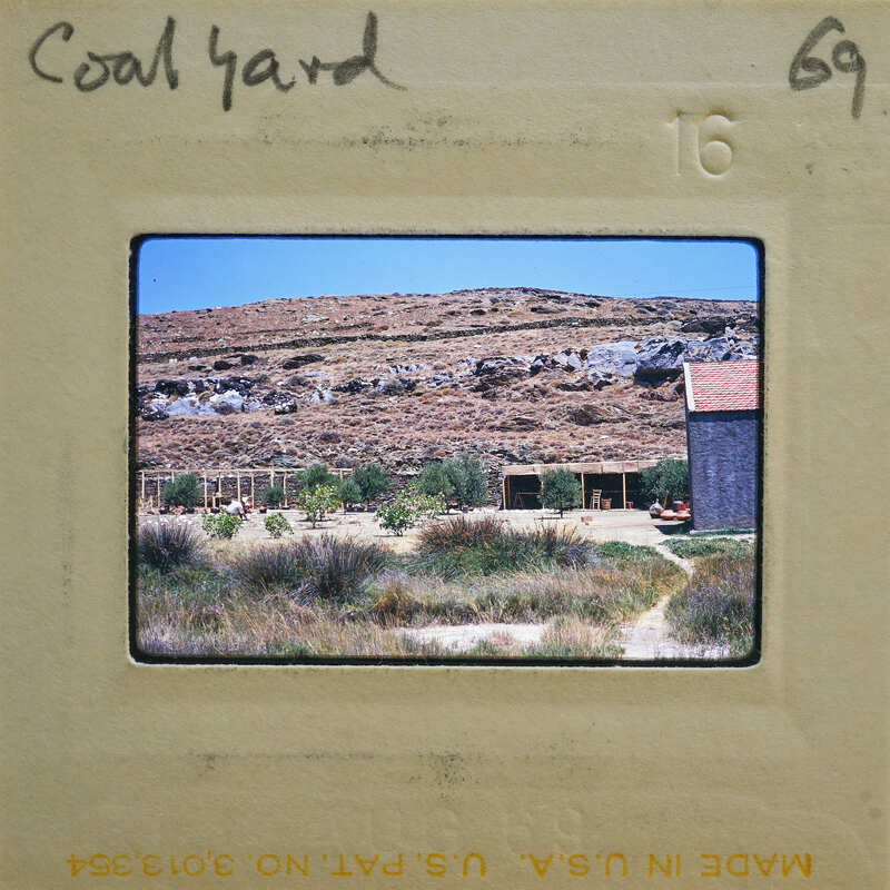 A photograph of a coal yard with mountains and buildings in the background.