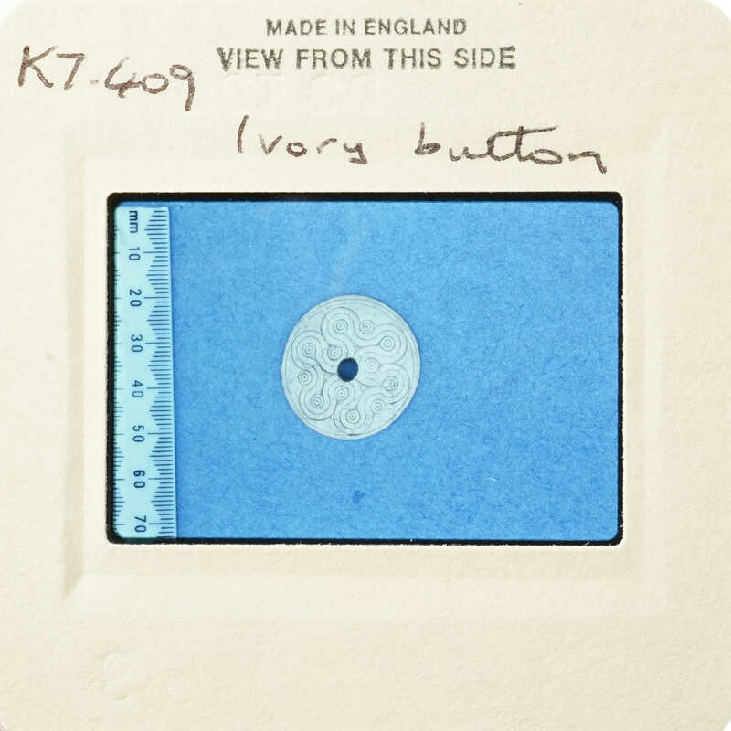 A circular object with intricate patterns, possibly an ivory button, on a blue background with measurements.