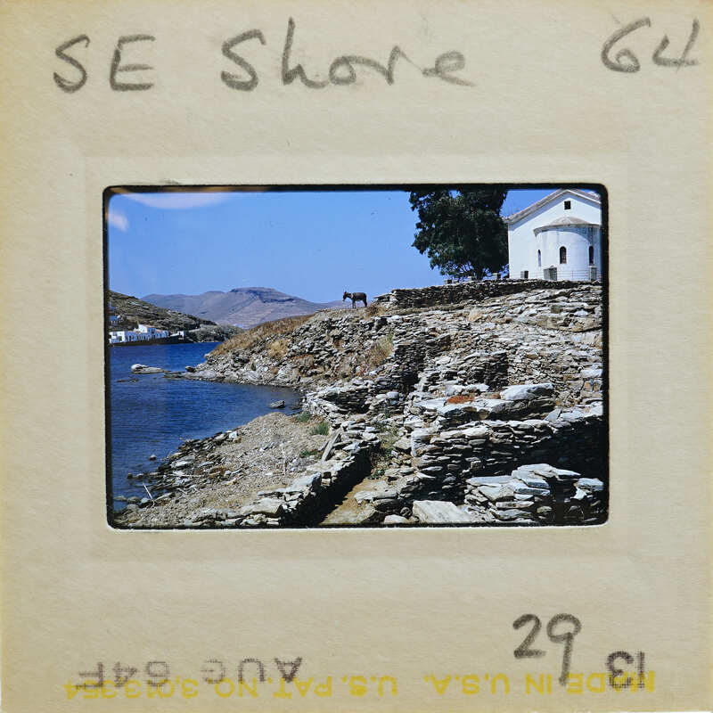 Picture of a coastal landscape with stone walls and water with white building on hill.