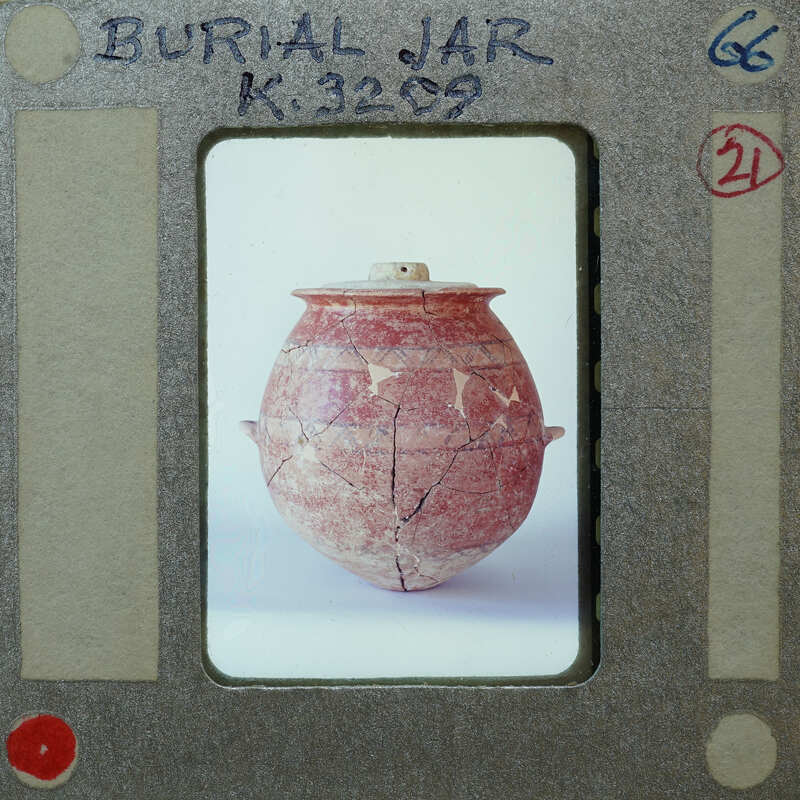 A photograph of a cracked clay pot with lid identified as a burial jar (K.3209).