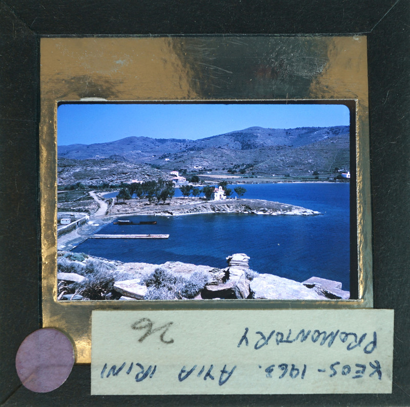 A vintage postcard with a photo of a coastal landscape, featuring a harbor and mountains, enclosed within a cardboard frame with handwritten text on the back.