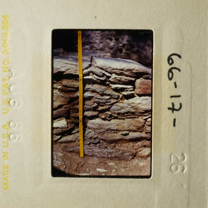 This is an image of a rock wall, possibly from an archaeological site, with a yellow measuring tape indicating its thickness.