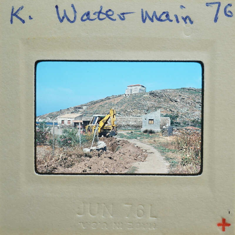 A photograph of a rural landscape with a dirt road, a building under construction, and a hillside.