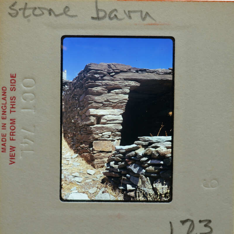 Old stone building on a hillside with grass and rocks around it.