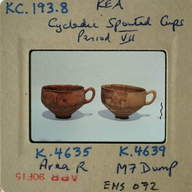 Two ancient Greek cups with handles and designs, displayed side by side on a white surface.