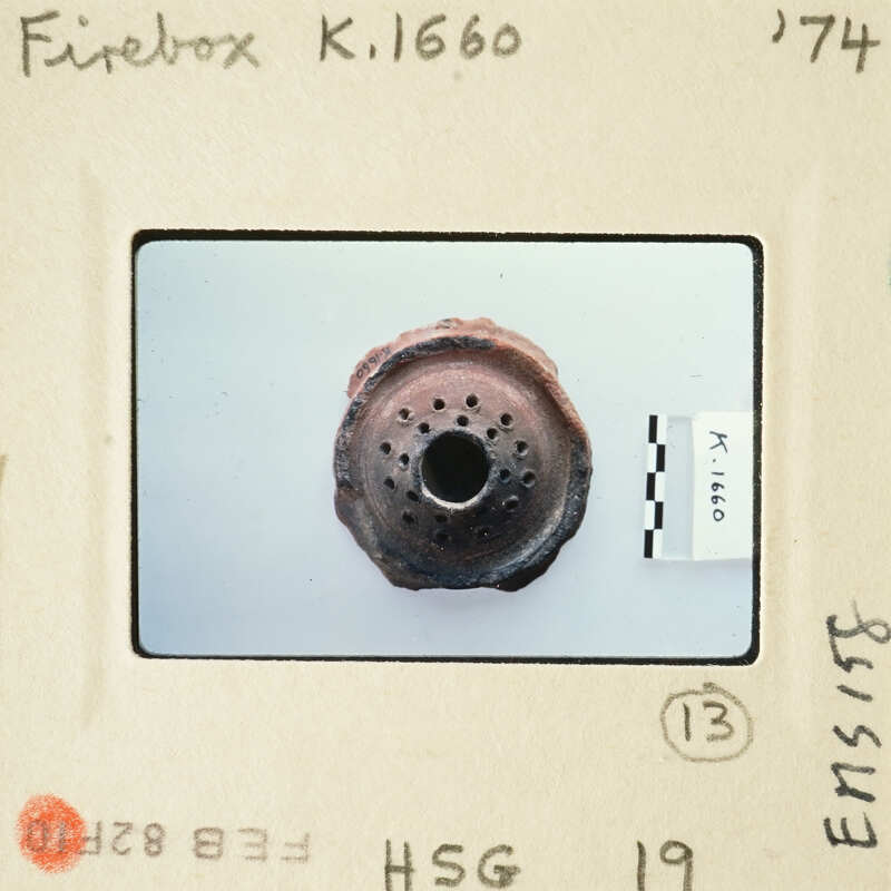 Old rusty metal object with holes, possibly an antique part, on a white background.