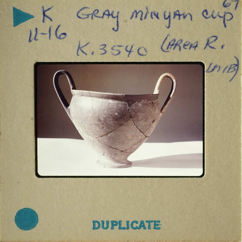 Ancient Greek vase with visible cracks and chips, displayed on a white surface.
