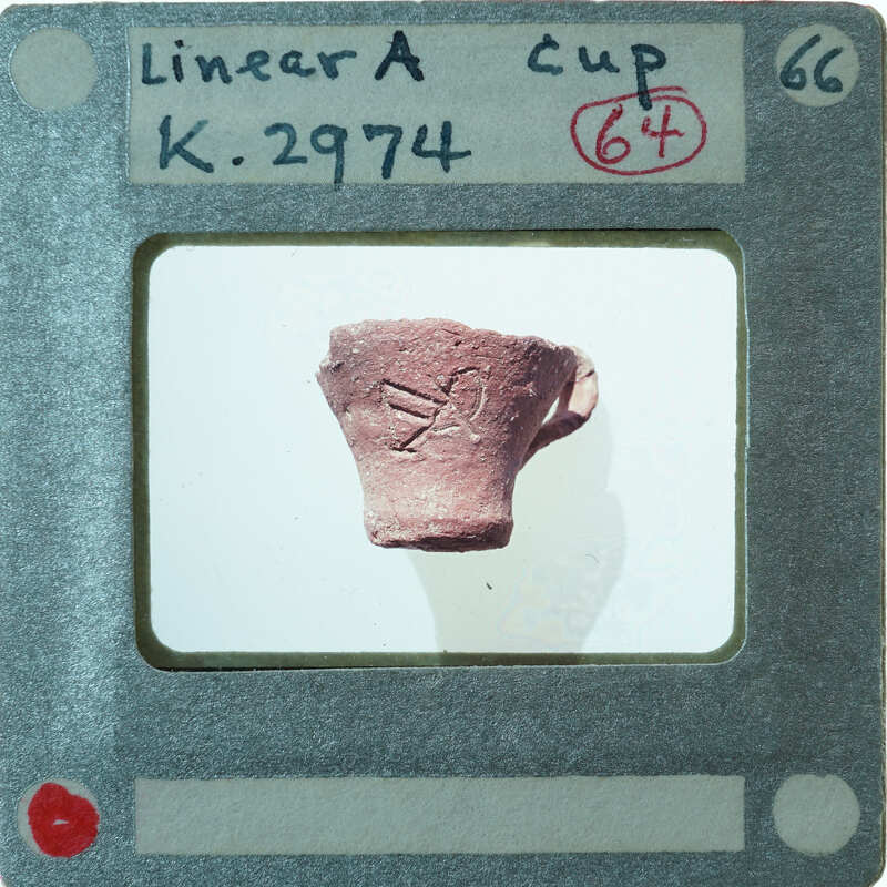 A photograph of a small, red clay pot with markings on it, K.2974.