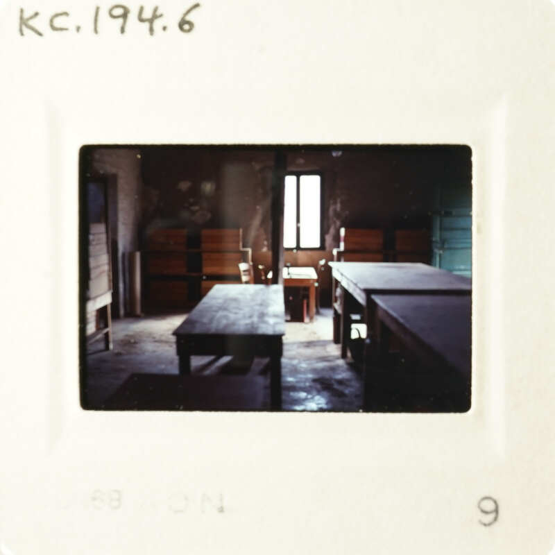 Photo of an empty room with tables and benches, taken from the perspective of someone standing outside the room.