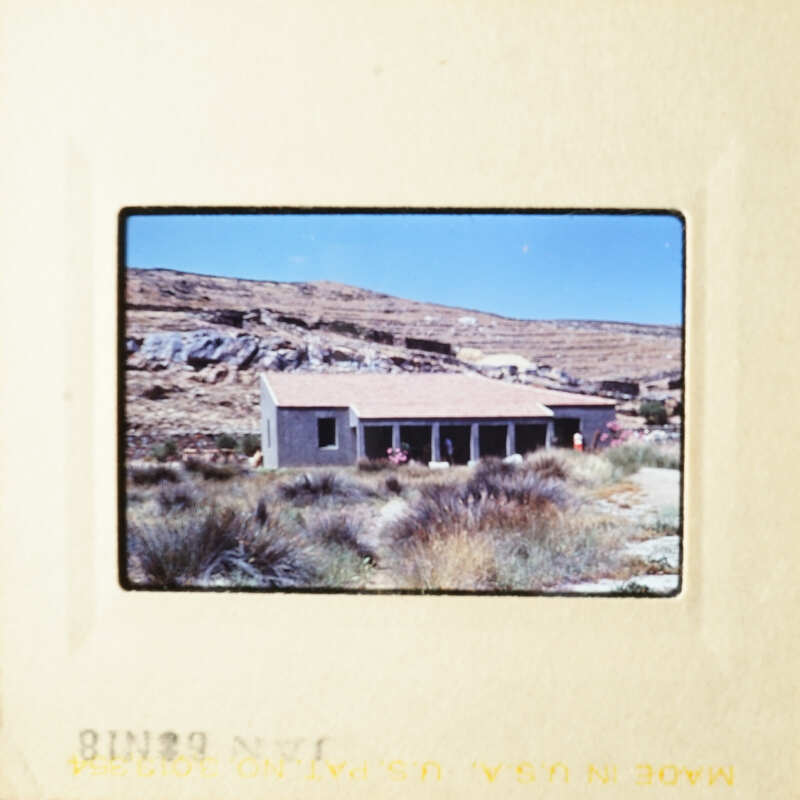 A small building with a dirt roof, surrounded by dry grass and mountains in the background.