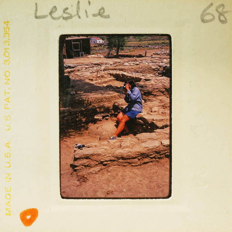 Woman sitting on stone ruins with a camera, taking a photo.