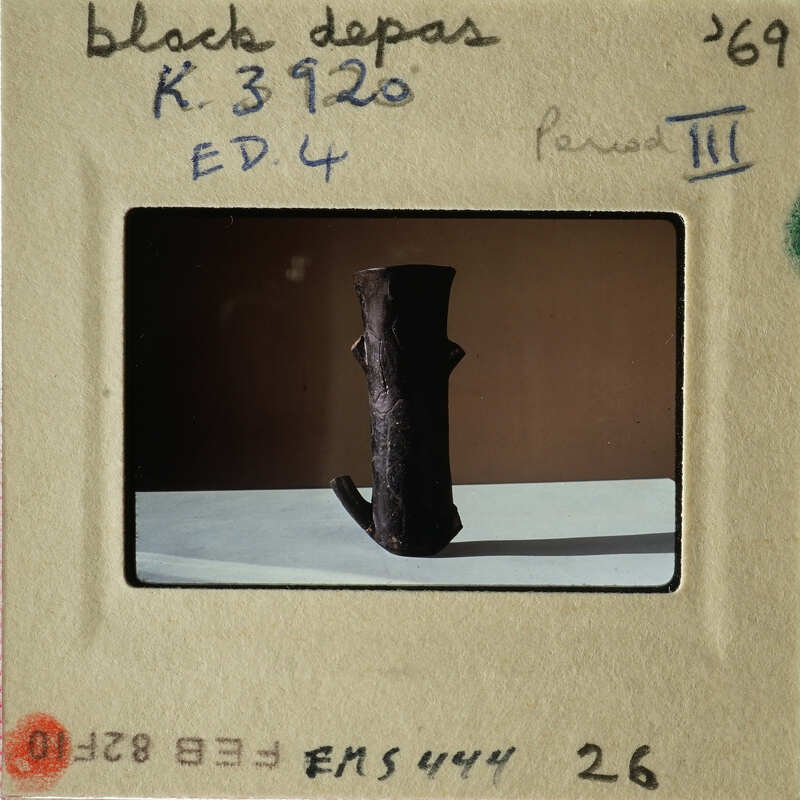 Brown clay sculpture on white surface with black border and handwritten label.