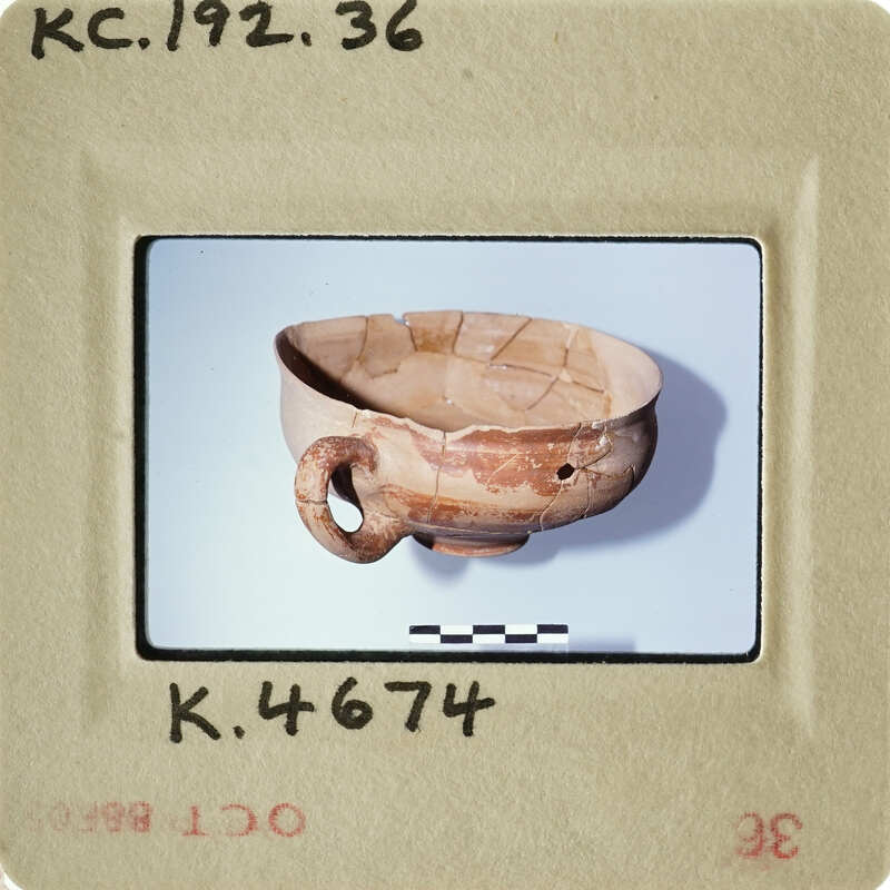 Ancient ceramic bowl with handle, displayed on white surface.
