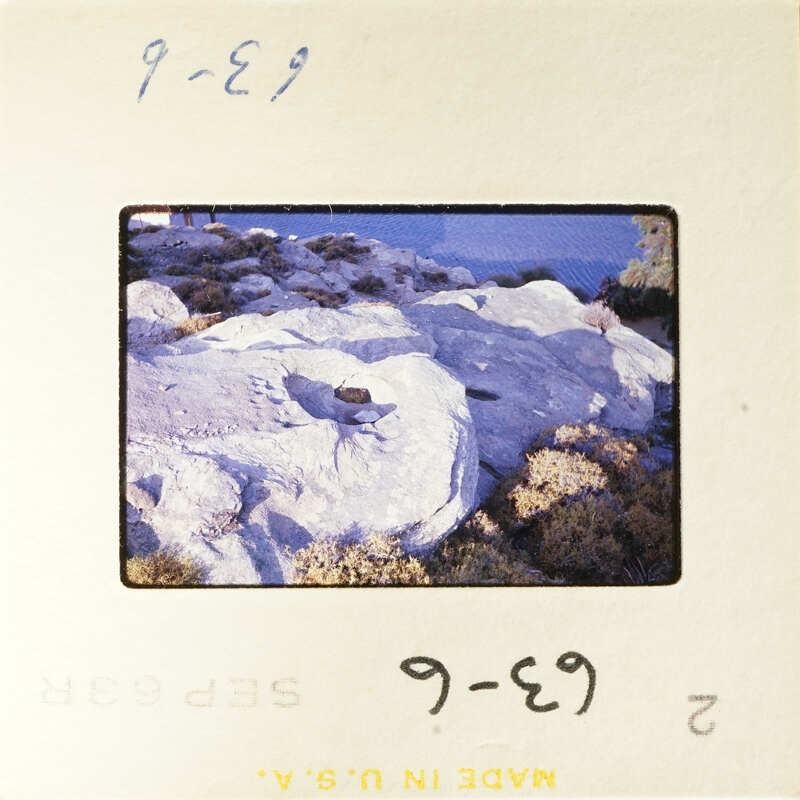 A photograph of a rocky cliff with vegetation at its base, taken during daylight.