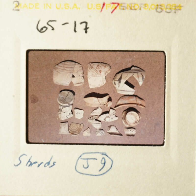 The image shows an archaeological artifact with various pieces, possibly pottery shards, on a table.