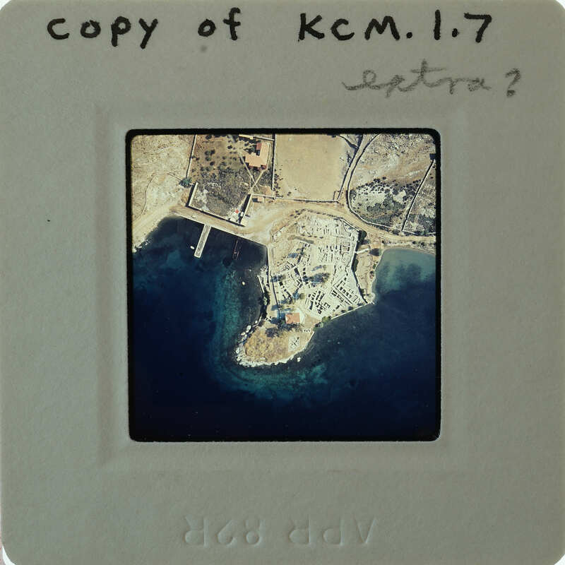 Aerial photograph of a coastal area with water and land features, enclosed by a white border on a film strip.