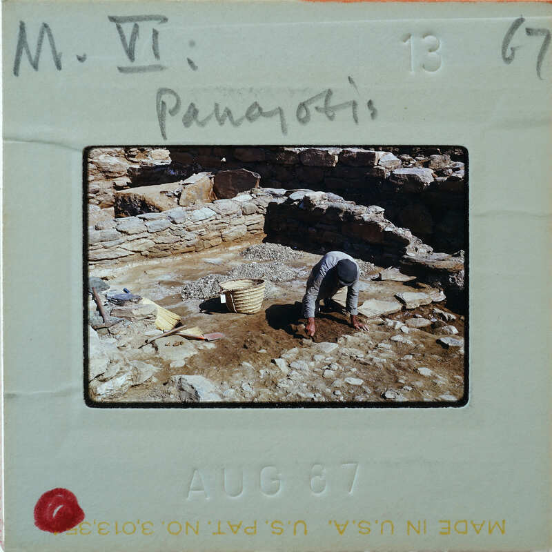 A man digging through an archaeological site with stone ruins and a bucket.