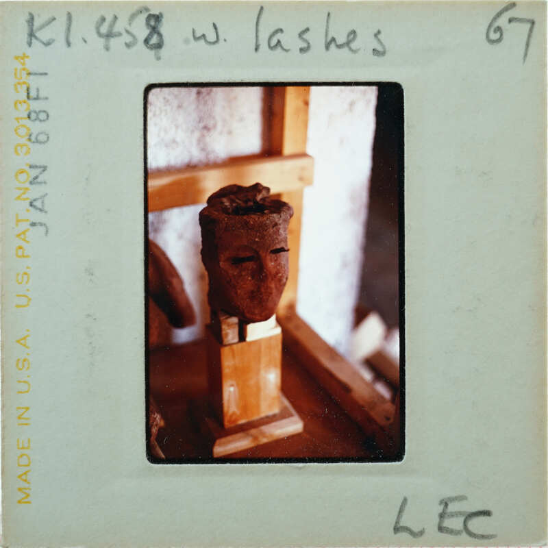 Terracotta head on wooden pedestal with drawn eyelashes.