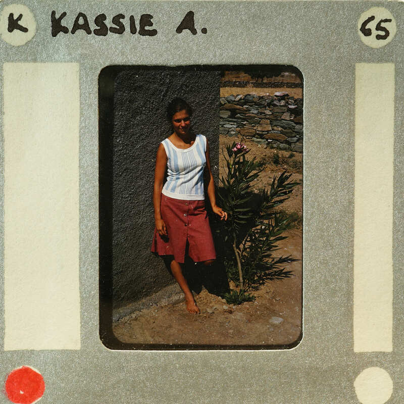 A woman standing outside with a plant behind her, captured on an old film strip.