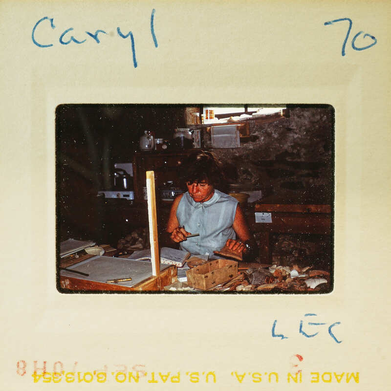 A woman working on a craft project at a table with various materials and tools around her.