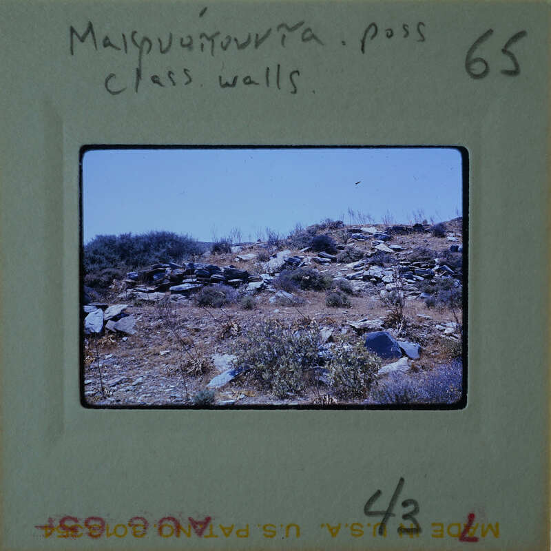 A photograph of a rocky hillside with sparse vegetation, taken from a distance and showing the sky above.