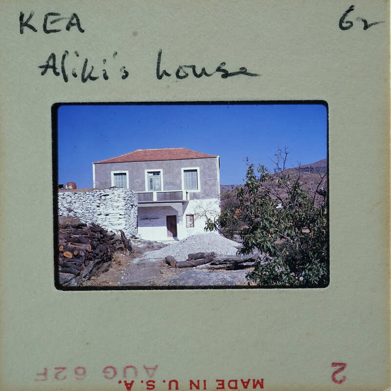 A photograph of a house with a stone wall and a wooden door, taken from the street level.