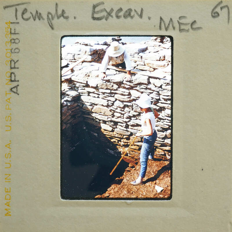 Photo of two people working on a stone structure.