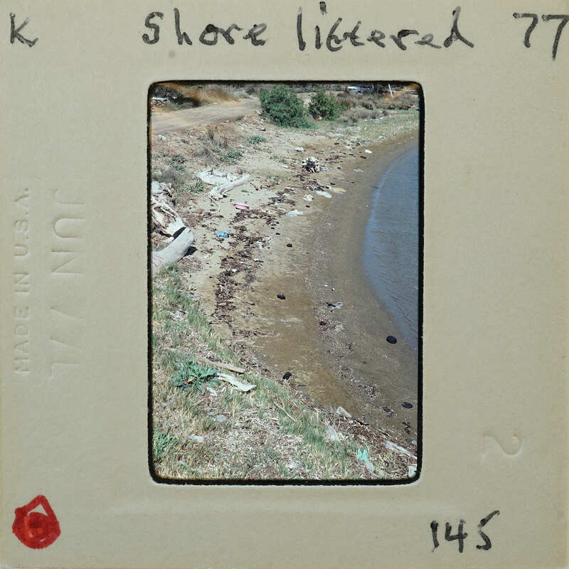 The image is a faded photograph of a shoreline with trash scattered on the beach, taken from an old film strip.