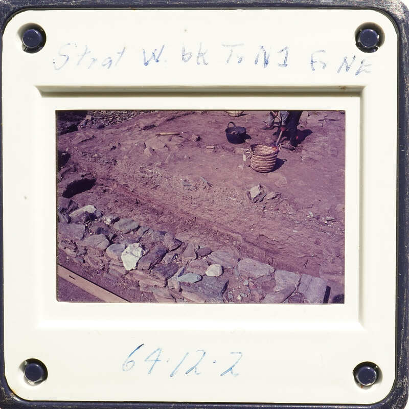Old photo of a rocky landscape with a stone wall and dirt ground, possibly from an archaeological site.