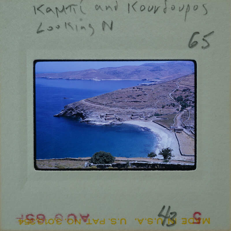 A vintage photo of a scenic coastal landscape with mountains and water, featuring two people looking out towards the sea.