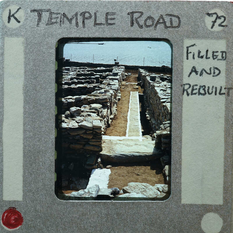 Picture of a stone-paved road with ruins and water in the background, framed as an old film strip.
