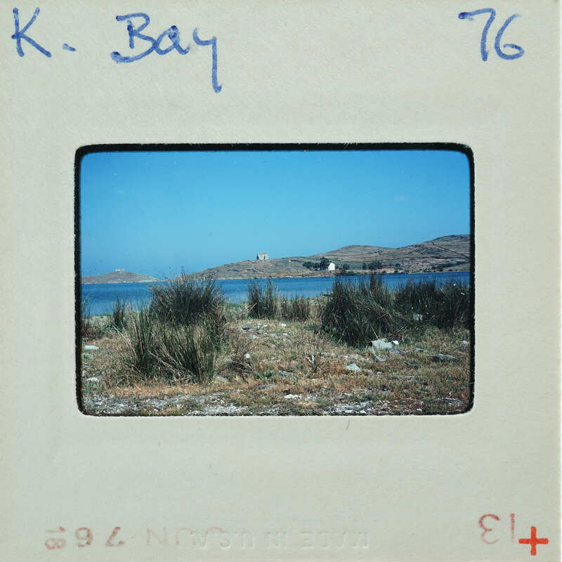 A vintage photograph of a serene coastal landscape with a body of water and vegetation, enclosed within an old film strip frame.