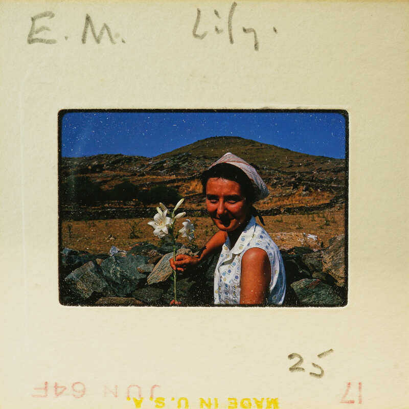A vintage photograph of a woman holding flowers, with mountains in the background.