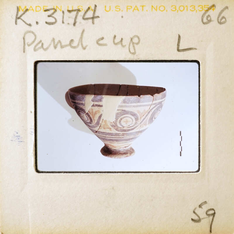 Ancient ceramic bowl with intricate patterns and a handle, displayed on a white surface.