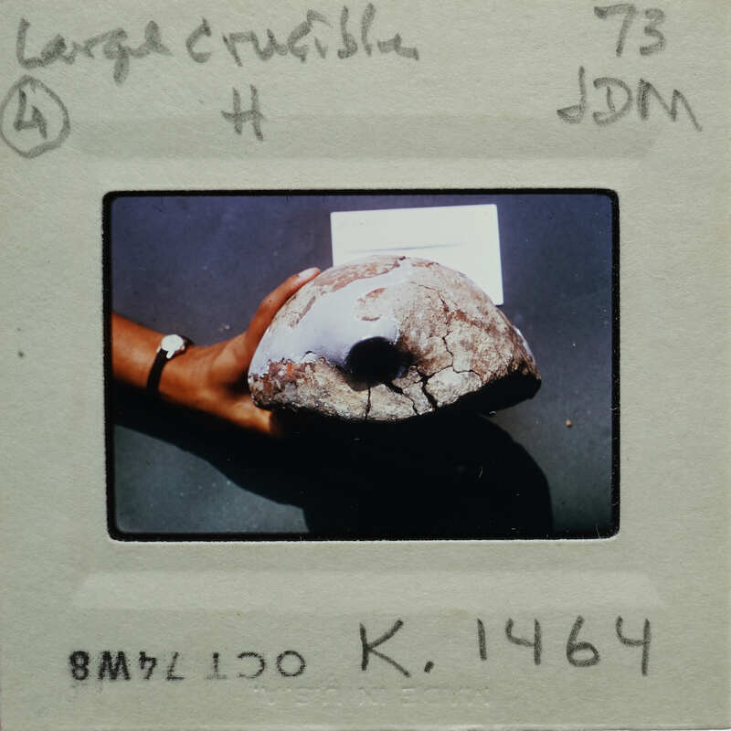 Hand holding a large, irregularly shaped object with rough texture and dark color.