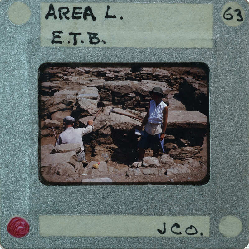A photograph of two archaeologists working at an excavation site, with a label indicating it's from Area L, E.T.B.