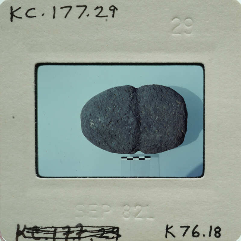 A black and white photo of a rock with an indentation, placed on a surface with a shadow cast to the right.