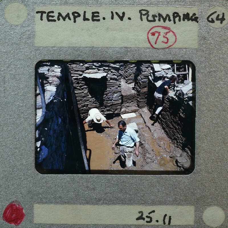 A photograph of archaeologists working at a site with water on the surface of the trench.