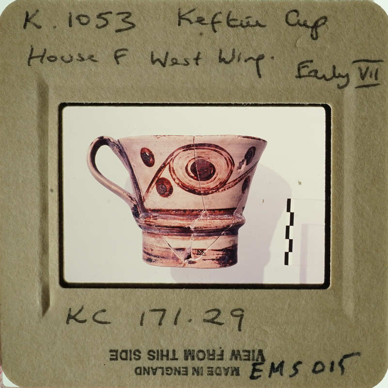 A photograph of an ancient Greek cup with intricate designs, displayed on a card.