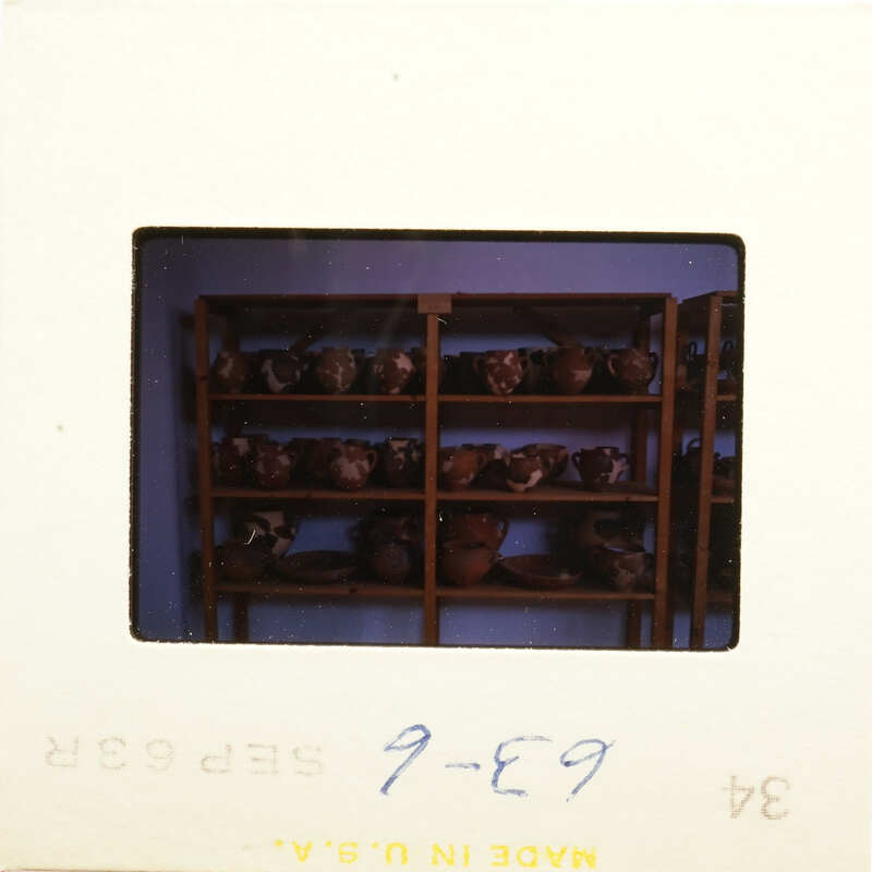 Photograph of pottery on shelves with blue writing on white background.