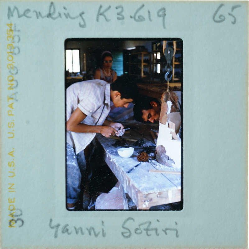 Two people at workbench restoring terracotta statue while another looks on.