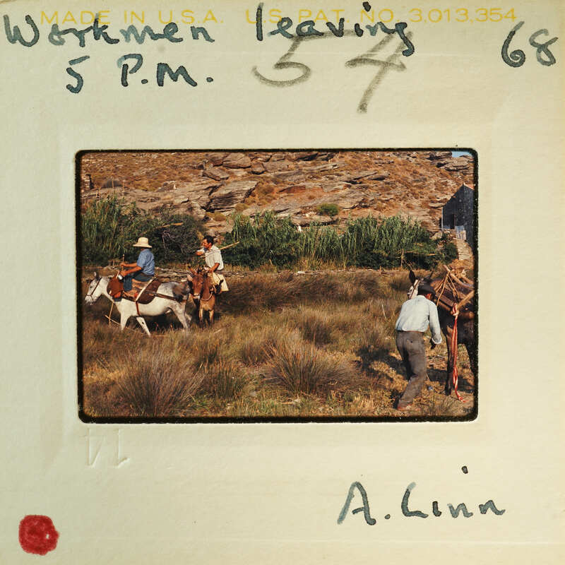 A vintage photograph of a man riding a horse, with another person walking beside him and a third person on foot behind them, set against a rocky landscape.