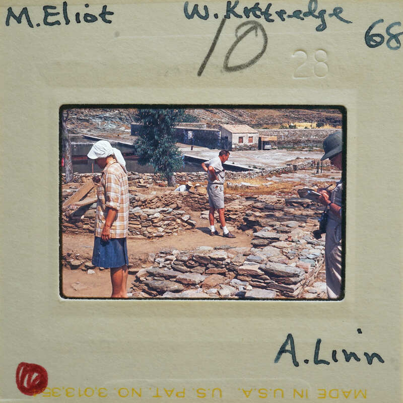 This is a vintage photograph of two people working on an archaeological site, with stone ruins and ancient artifacts visible.