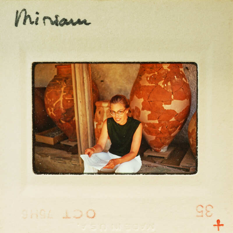 Woman sitting cross-legged with a smile, surrounded by large clay pots.