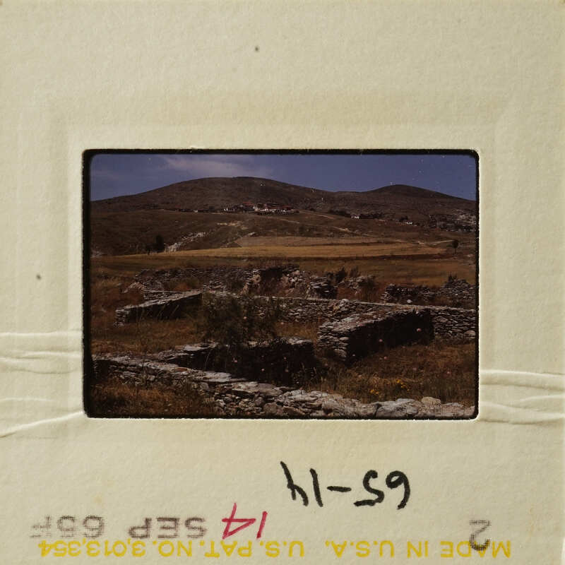 Stone ruins on hillside with grass and sky.