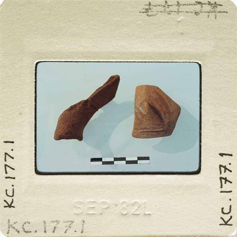 Two ancient clay objects on display, possibly artifacts with labels and measurements.