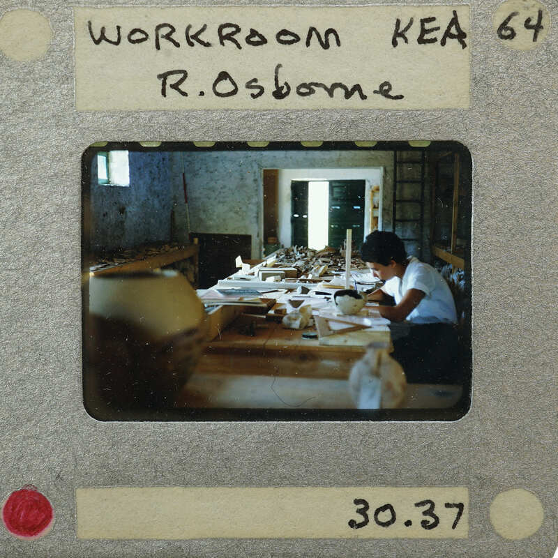 An old photograph of a person working at a desk with various items on it, labeled as "WORKSHOP KEAE 64" and identified by the number "30.287".