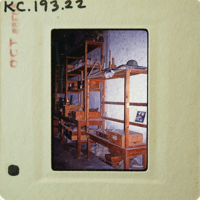 A vintage photograph of a workshop with wooden shelves and various tools and objects on them, enclosed within an old-fashioned film negative frame.