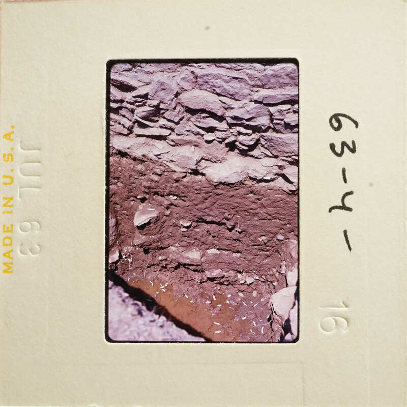 Photograph showing an aerial view of a rocky landscape with patches of dirt and vegetation, captured on an old film slide.